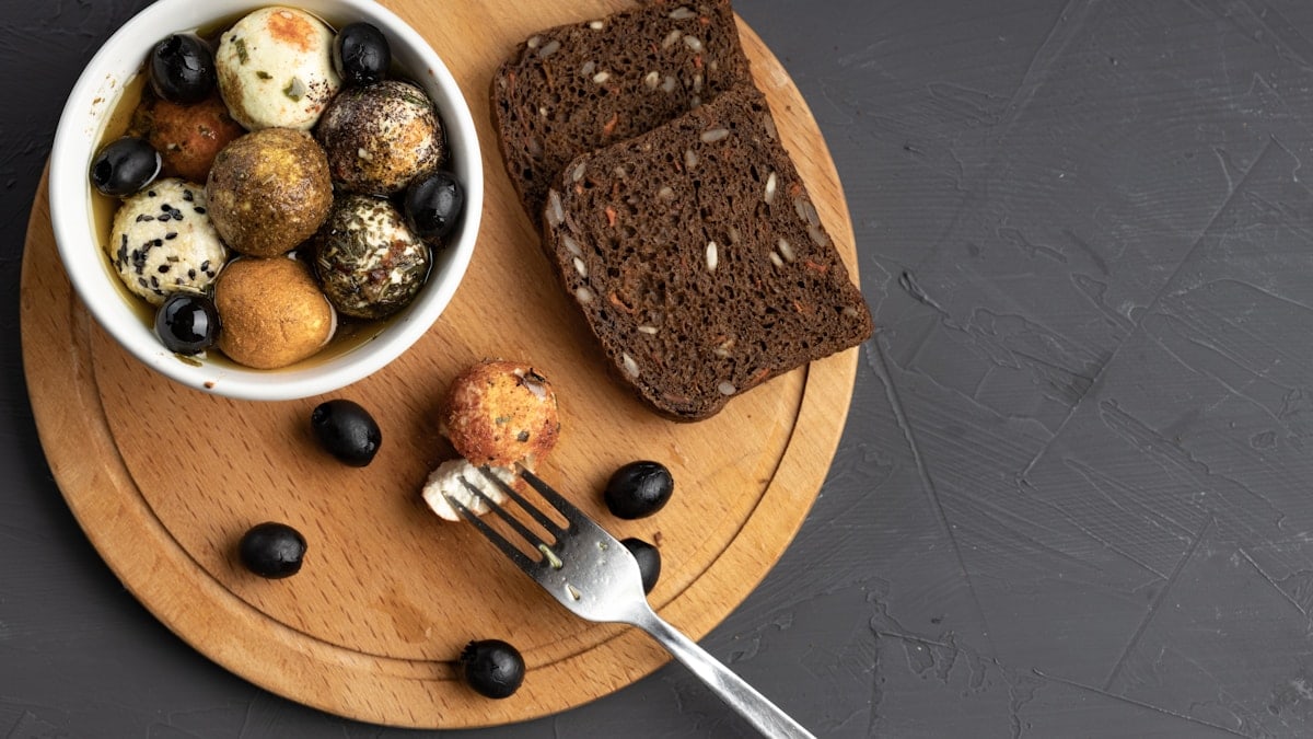 spicy cheese balls in butter next to a fork and bread on a curved cutting board